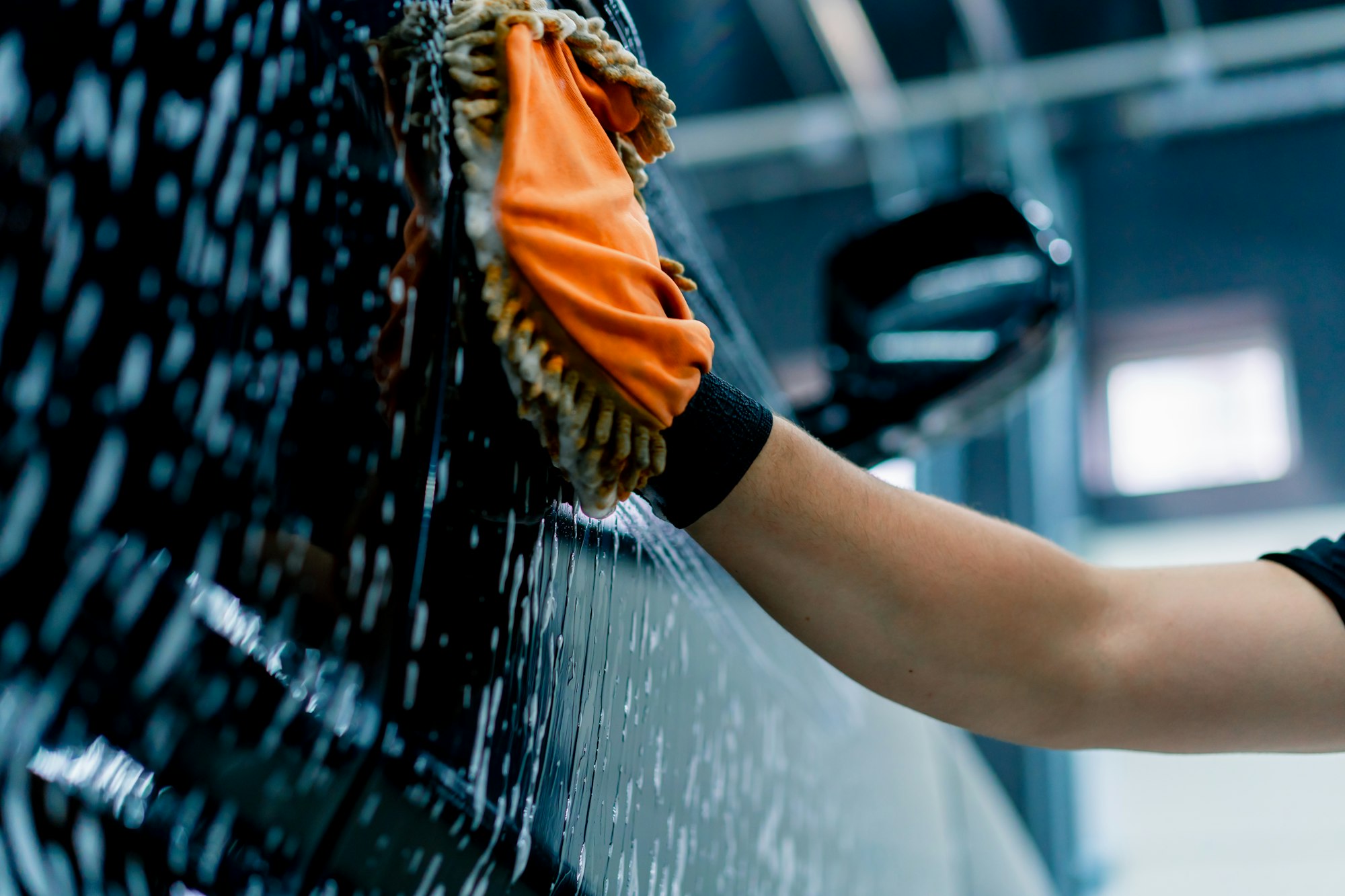 Close-up of a car wash worker using a microfiber cloth to wash black luxury car with wash shampoo